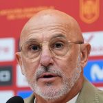 Luis de la Fuente, con gafas y chaqueta beis, habla ante el micrófono delante del panel de patrocinadores de la selección