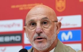 Luis de la Fuente, con gafas y chaqueta beis, habla ante el micrófono delante del panel de patrocinadores de la selección
