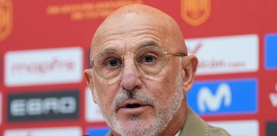 Luis de la Fuente, con gafas y chaqueta beis, habla ante el micrófono delante del panel de patrocinadores de la selección