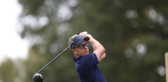 Luke Donald, con visera y gafas de sol, sigue la trayectoria de su golpe con el driver tras la salida en un tee arbolado