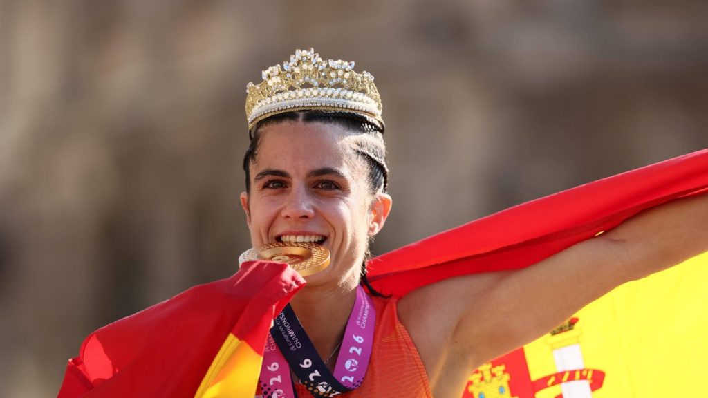 María Pérez, con una corona dorada y la bandera de España a la espalda, muerde su medalla de oro