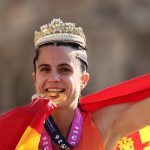 María Pérez, con una corona dorada y la bandera de España a la espalda, muerde su medalla de oro