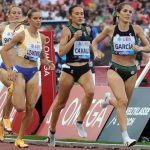 Marta García, con top verde y negro, encabeza a un grupo de corredoras en la recta de la pista, con la grada llena al fondo