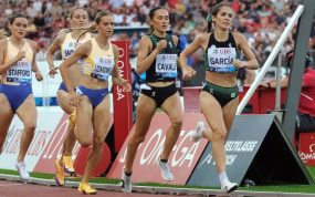 Marta García, con top verde y negro, encabeza a un grupo de corredoras en la recta de la pista, con la grada llena al fondo