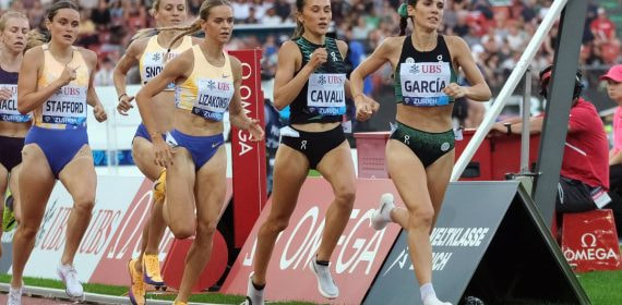 Marta García, con top verde y negro, encabeza a un grupo de corredoras en la recta de la pista, con la grada llena al fondo