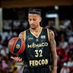 Matthew Strazel, con la camiseta negra y dorada del Mónaco, deja el balón suspendido sobre la palma de la mano en un pabellón