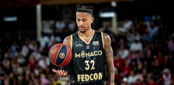 Matthew Strazel, con la camiseta negra y dorada del Mónaco, deja el balón suspendido sobre la palma de la mano en un pabellón