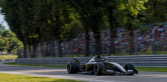 Un monoplaza pasa a toda velocidad junto a una grada llena en un circuito rodeado de árboles