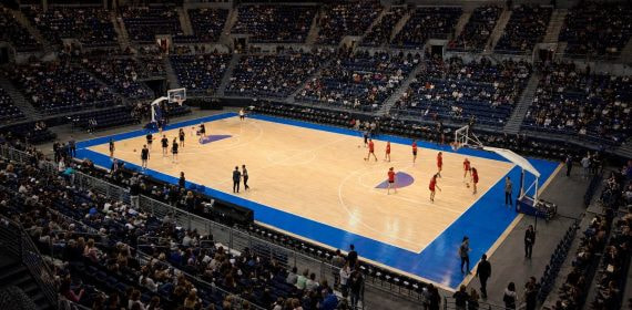 Vista elevada de una pista de baloncesto en un pabellón cubierto durante el calentamiento previo a un partido internacional