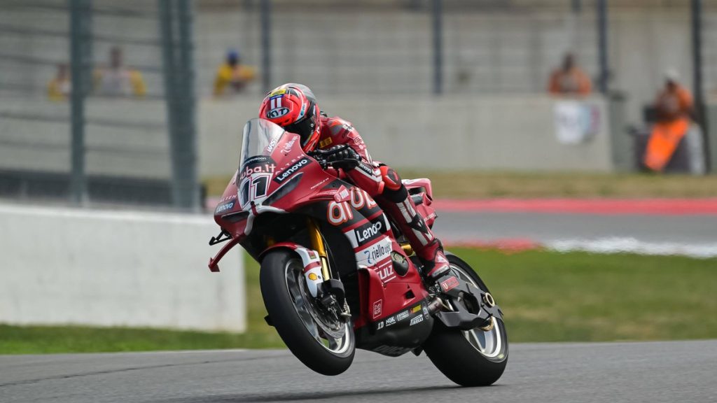 Nicolò Bulega, con mono y casco rojos, levanta la rueda delantera de la Ducati número 11 al salir de una curva
