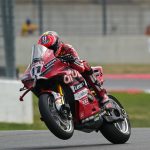Nicolò Bulega, con mono y casco rojos, levanta la rueda delantera de la Ducati número 11 al salir de una curva