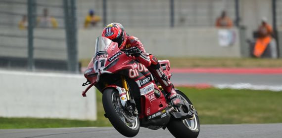 Nicolò Bulega, con mono y casco rojos, levanta la rueda delantera de la Ducati número 11 al salir de una curva