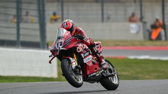Nicolò Bulega, con mono y casco rojos, levanta la rueda delantera de la Ducati número 11 al salir de una curva