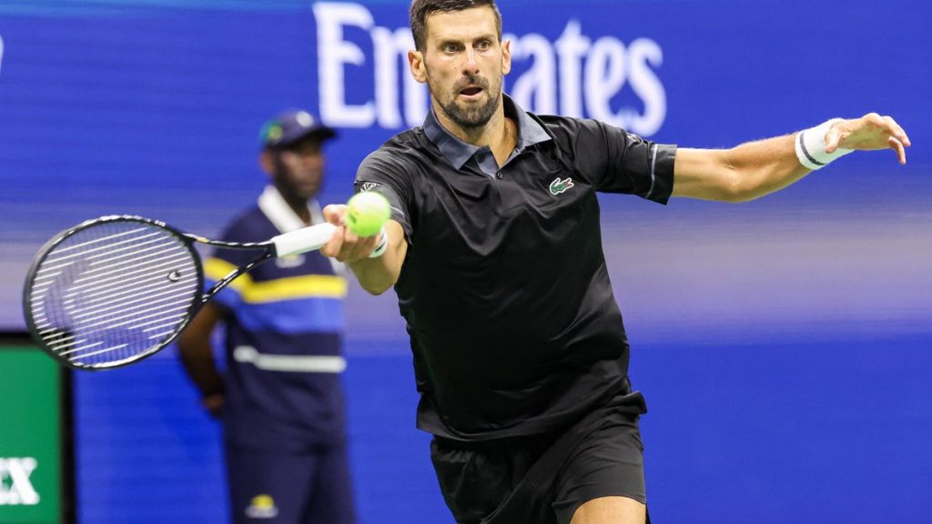 Novak Djokovic, con polo negro, estira el brazo para golpear una derecha con la pelota a la altura de la raqueta
