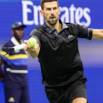 Novak Djokovic, con polo negro, estira el brazo para golpear una derecha con la pelota a la altura de la raqueta