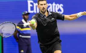 Novak Djokovic, con polo negro, estira el brazo para golpear una derecha con la pelota a la altura de la raqueta