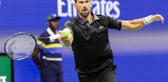 Novak Djokovic, con polo negro, estira el brazo para golpear una derecha con la pelota a la altura de la raqueta