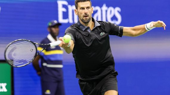 Novak Djokovic, con polo negro, estira el brazo para golpear una derecha con la pelota a la altura de la raqueta