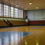 Interior de un pabellón municipal de baloncesto con gradas de madera y media luz