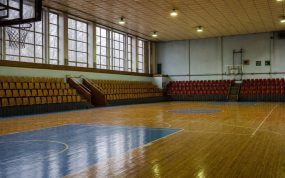 Interior de un pabellón municipal de baloncesto con gradas de madera y media luz