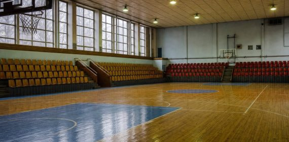 Interior de un pabellón municipal de baloncesto con gradas de madera y media luz