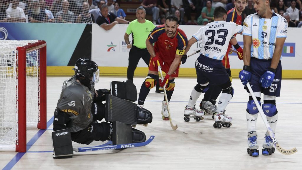 Un jugador de hockey patines de rojo celebra con el stick en la mano ante el portero rival agachado junto a la portería