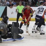 Un jugador de hockey patines de rojo celebra con el stick en la mano ante el portero rival agachado junto a la portería