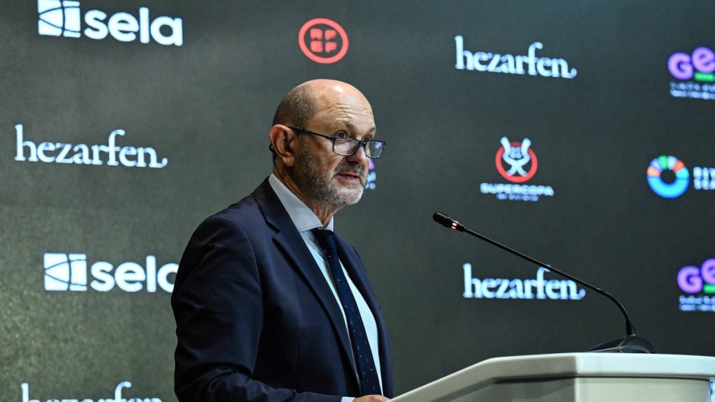 Rafael Louzán, con gafas y traje azul marino, habla desde un atril ante un panel de patrocinadores con el logo de la Supercopa