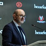 Rafael Louzán, con gafas y traje azul marino, habla desde un atril ante un panel de patrocinadores con el logo de la Supercopa
