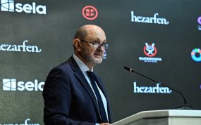 Rafael Louzán, con gafas y traje azul marino, habla desde un atril ante un panel de patrocinadores con el logo de la Supercopa