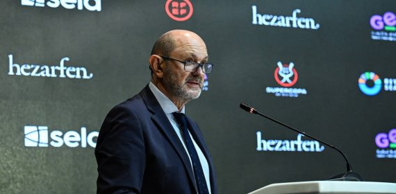 Rafael Louzán, con gafas y traje azul marino, habla desde un atril ante un panel de patrocinadores con el logo de la Supercopa