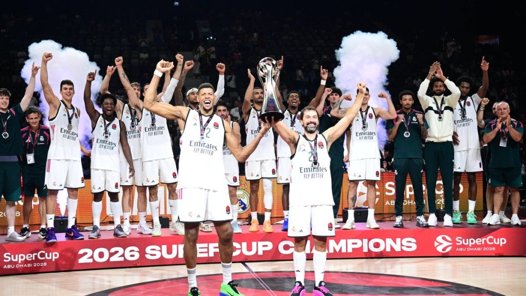 Los jugadores del Real Madrid, con camiseta blanca, levantan los brazos alrededor del trofeo en el podio de campeones de la SuperCup