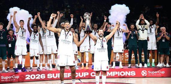 Los jugadores del Real Madrid, con camiseta blanca, levantan los brazos alrededor del trofeo en el podio de campeones de la SuperCup