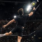 Un jugador de pádel, de espaldas y en el aire, estira el brazo para rematar la bola ante una grada llena