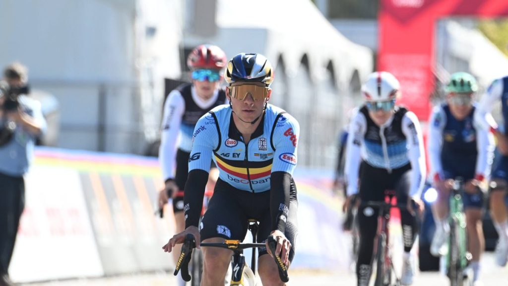 Un ciclista con el maillot celeste de Bélgica y gafas doradas rueda en cabeza de un grupo junto a las vallas del circuito