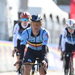 Un ciclista con el maillot celeste de Bélgica y gafas doradas rueda en cabeza de un grupo junto a las vallas del circuito
