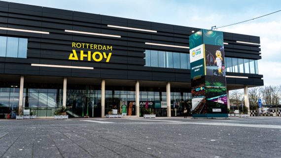 Fachada negra del pabellón Rotterdam Ahoy con su rótulo amarillo y una columna publicitaria delante de la entrada acristalada
