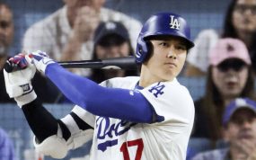 Un bateador de los Dodgers con casco azul y el dorsal 17 sigue con la mirada la bola tras golpearla, con el público detrás