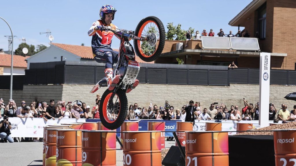 Toni Bou, con casco y mono de Repsol, salta con su moto de trial sobre una fila de barriles naranjas ante el público