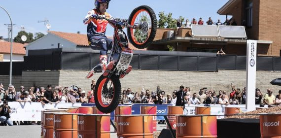 Toni Bou, con casco y mono de Repsol, salta con su moto de trial sobre una fila de barriles naranjas ante el público