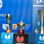 Los trofeos de la Copa de la Reina, la Supercopa y la Liga Femenina Endesa sobre tres pedestales ante un fondo azul