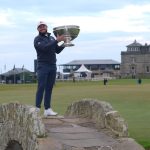Tyrrell Hatton levanta el trofeo de pie sobre un puente de piedra del Old Course, con la casa club al fondo