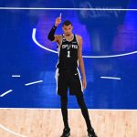 Victor Wembanyama, con la camiseta negra de los Spurs, levanta el dedo índice de pie en la zona de la pista