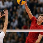 Un jugador de voleibol remata el balón por encima de la red ante el bloqueo de un rival