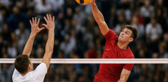 Un jugador de voleibol remata el balón por encima de la red ante el bloqueo de un rival