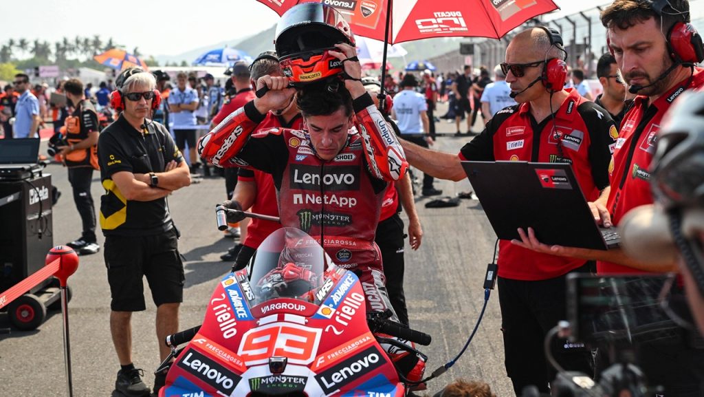 Marc Márquez se quita el casco, sentado en su moto en la parrilla de salida, junto a dos miembros del equipo Ducati durante el Gran Premio de Indonesia de MotoGP.