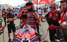 Marc Márquez se quita el casco, sentado en su moto en la parrilla de salida, junto a dos miembros del equipo Ducati durante el Gran Premio de Indonesia de MotoGP.
