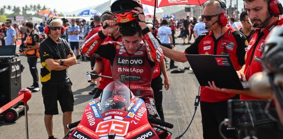 Marc Márquez se quita el casco, sentado en su moto en la parrilla de salida, junto a dos miembros del equipo Ducati durante el Gran Premio de Indonesia de MotoGP.