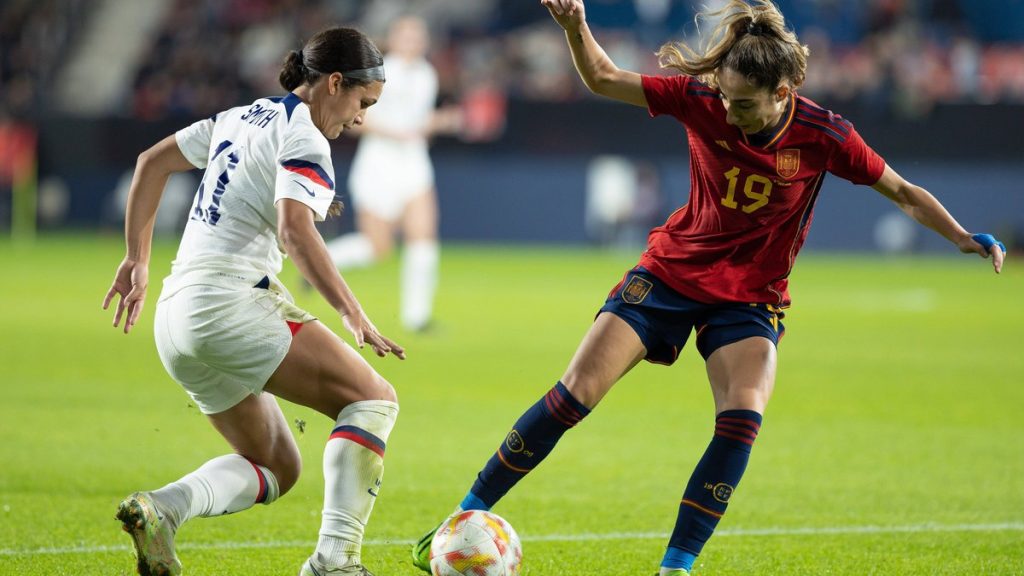 Olga Carmona, de rojo, protege el balón ante Sophia Smith, de blanco, sobre el césped