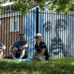 Aficionados del Manchester City sentados delante de un mural de Pep Guardiola durante la celebración del título de Premier League 2025/26.